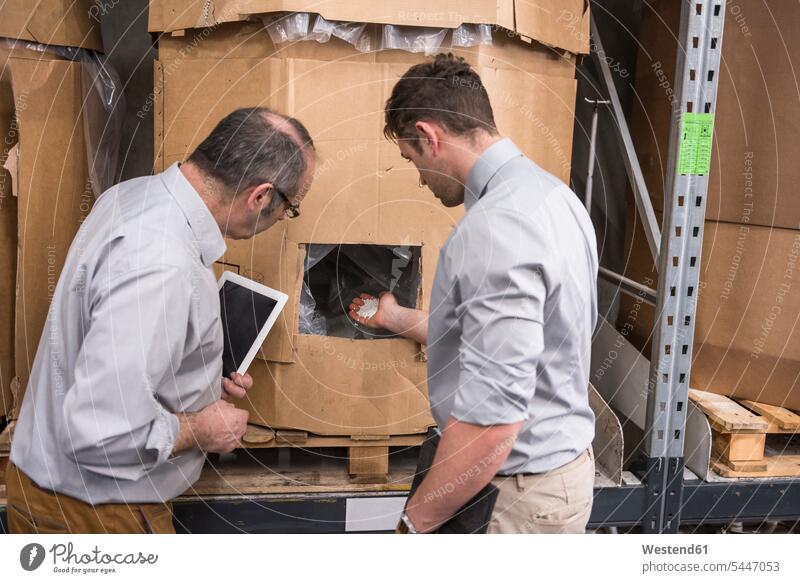 Two men examining product in factory warehouse talking speaking colleagues factories man males Adults grown-ups grownups adult people persons human being humans