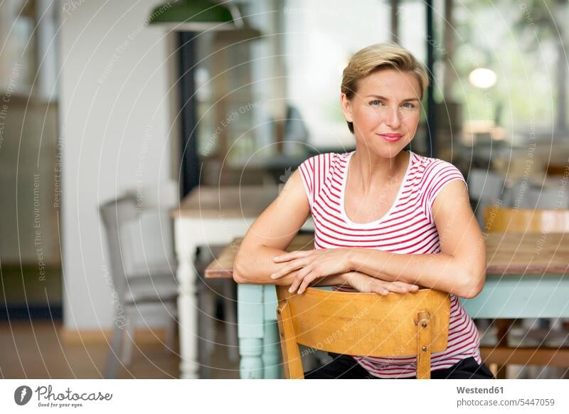 Portrait of confident blond woman sitting on chair smiling smile businesswoman businesswomen business woman business women females Seated portrait portraits
