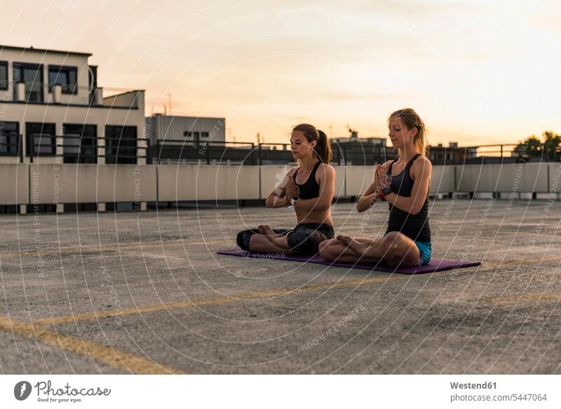 Two women practicing yoga on parking level in the city female friends sitting Seated woman females mate friendship Adults grown-ups grownups adult people