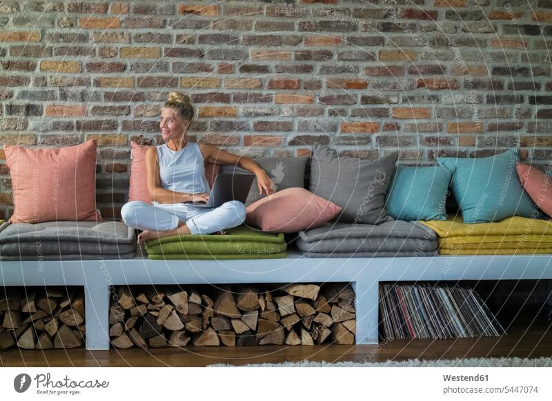 Mature woman sitting on couch, usine laptop Seated country house country houses cottage cottages Country Cottage home at home working At Work settee sofa sofas