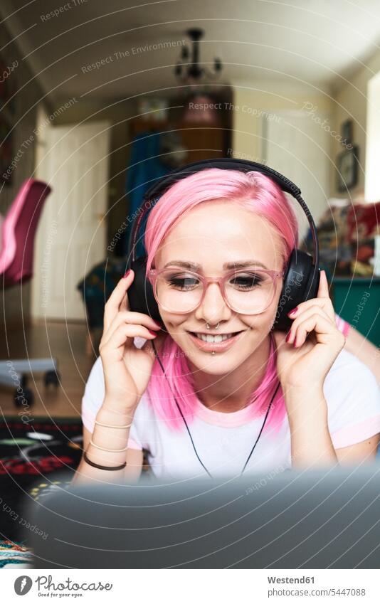 Young woman with pink hair listening to music via laptop at home females women headphones headset glasses specs Eye Glasses spectacles Eyeglasses cheerful
