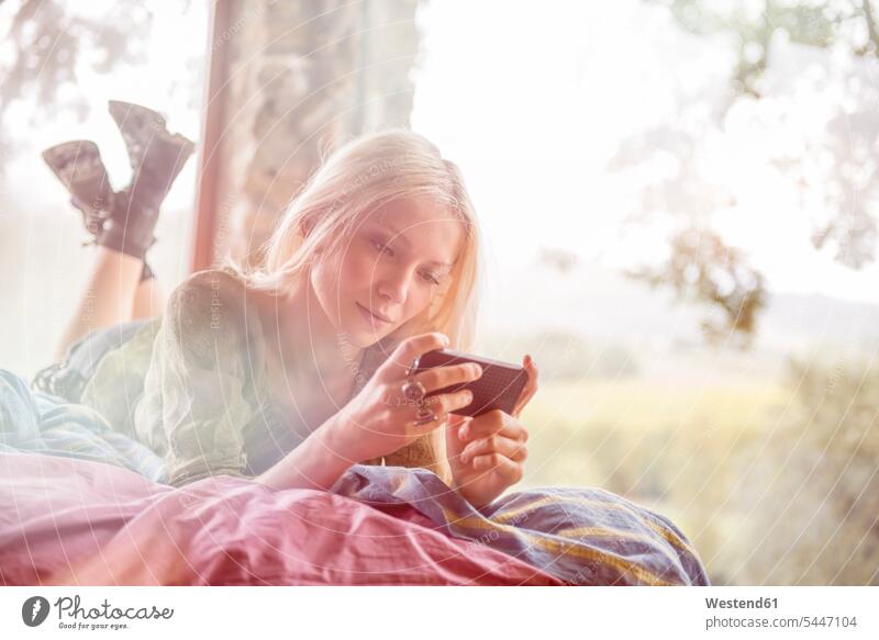 Portrait of young woman lying on bed looking at cell phone females women Smartphone iPhone Smartphones Adults grown-ups grownups adult people persons