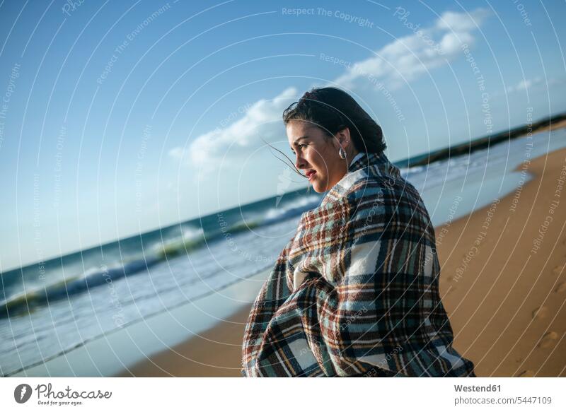 Young woman with blanket on the beach looking at the se beaches females women Adults grown-ups grownups adult people persons human being humans human beings