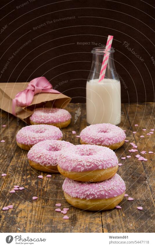 Doughnuts with pink icing and sugar granules and a bottle of milk on wood bow bows wooden rustic on top of sweet Sugary sweets doughnut donuts sugar icing