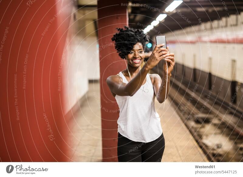 USA, New York City, Manhattan, smiling woman taking selfie at subway station platform females women Selfie Selfies waiting Smartphone iPhone Smartphones Adults