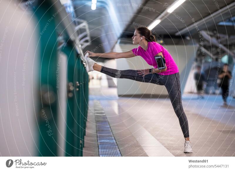 Young woman in pink sportshirt listening to music and stretching in urban metro station young women young woman jogger joggers female jogger exercising exercise