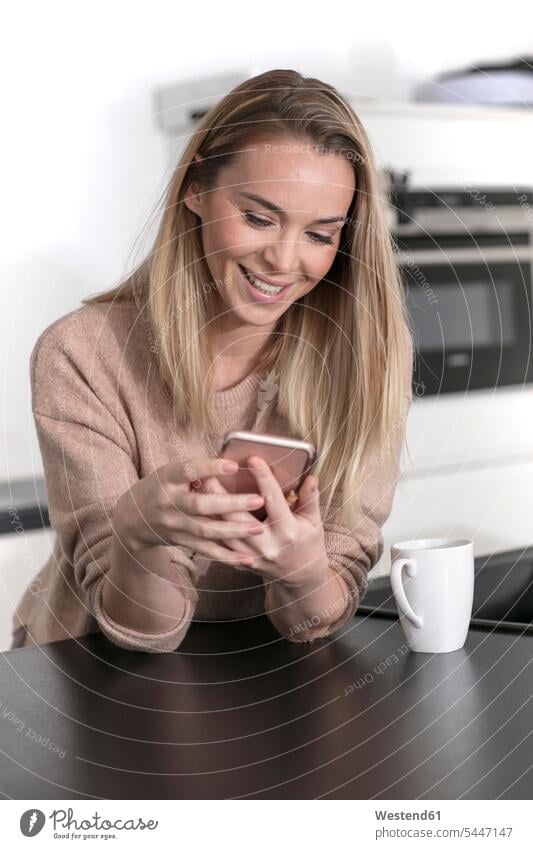 Portrait of smiling blond woman using cell phone at home blond hair blonde hair Smartphone iPhone Smartphones use portrait portraits females women people