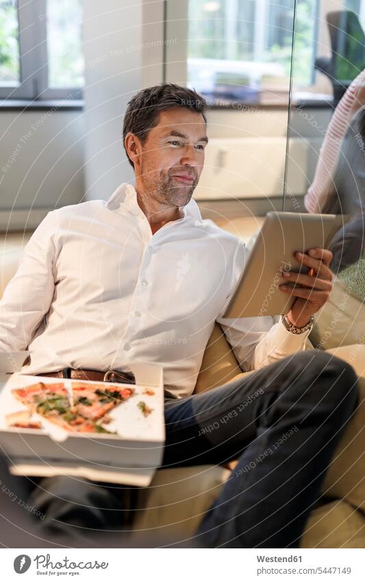 Businessman in bean bag in office eating pizza and using tablet Business man Businessmen Business men Pizza Pizzas sitting Seated digitizer Tablet Computer