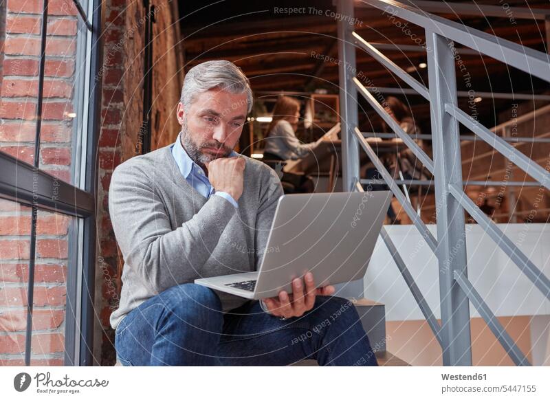 Businessman sitting on stairs of modern office, using laptop contemporary Seated working At Work offices office room office rooms loft lofts Business man