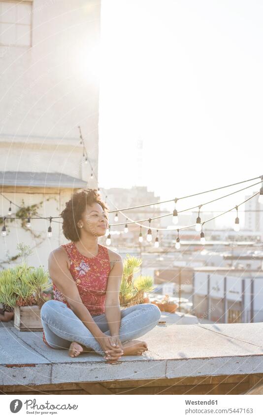 Young woman sitting on rooftop terrace, enjoying the sun cross-legged tailor seat thinking Seated roof terrace deck relaxation relaxing females women Adults