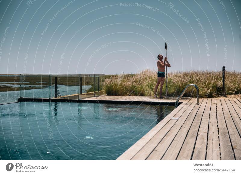 Man taking a shower on the edge of a modern infinity swimming pool man men males pools swimming pools Adults grown-ups grownups adult people persons human being