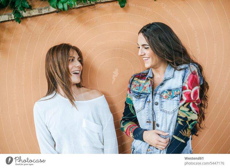 Two laughing friends in front of wall female friends walls Laughter mate friendship positive Emotion Feeling Feelings Sentiments Emotions emotional beautiful