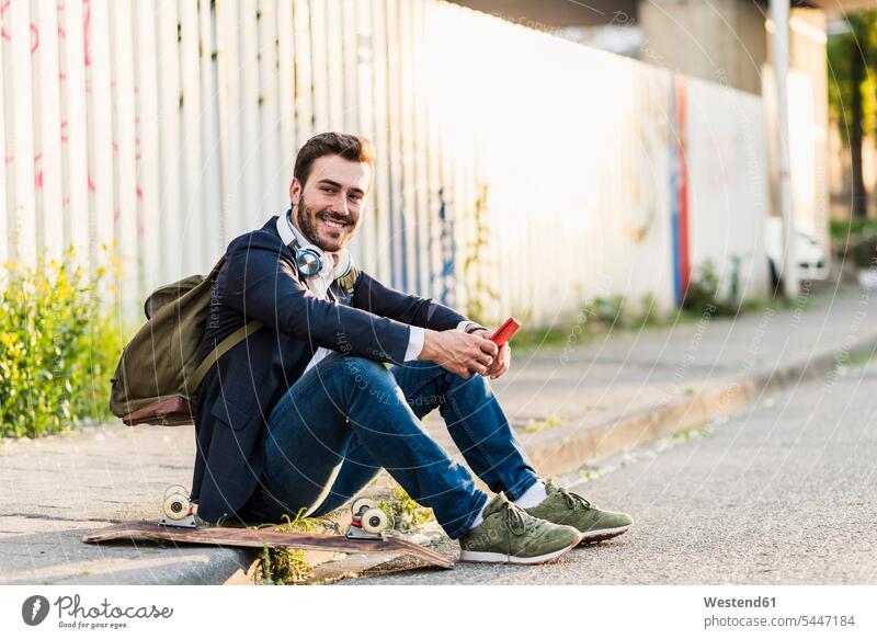 Smiling young man sitting on pavement holding cell phone smiling smile Seated males mobile phone mobiles mobile phones Cellphone cell phones Adults grown-ups