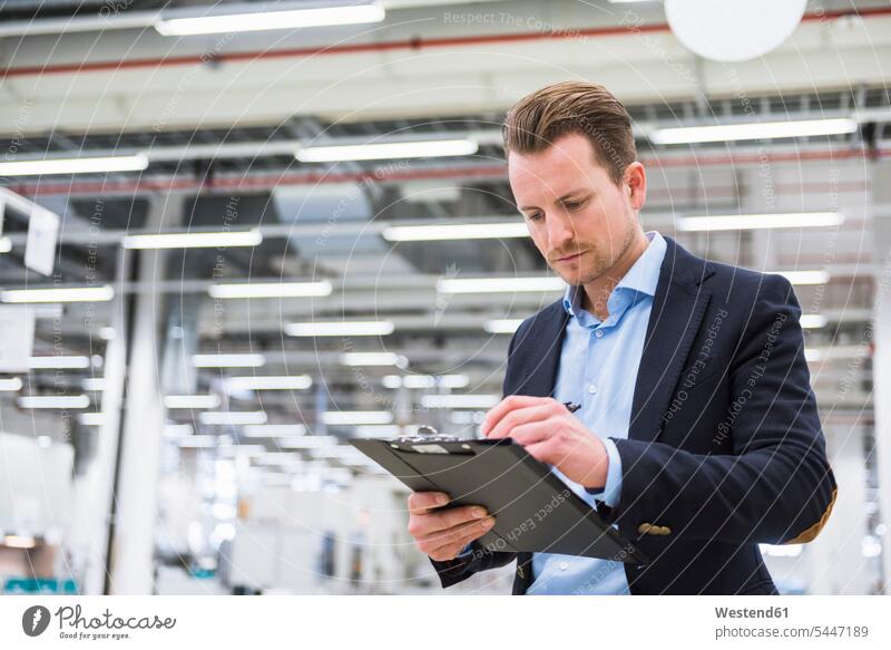 Man standing in factory shop floor taking notes making a note note taking man men males factories Adults grown-ups grownups adult people persons human being