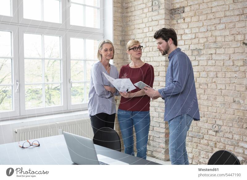 Mature businesswoman working with younger colleague in office talking speaking sharing share laptop Laptop Computers laptops notebook standing discussing