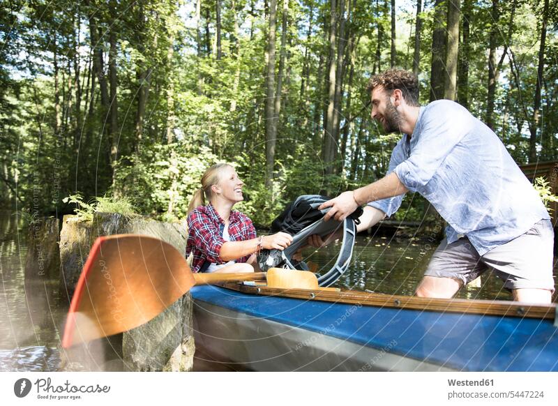 Happy young couple entering canoe in a forest brook getting in getting into board boarding woods forests happiness happy brooks rivulet twosomes partnership