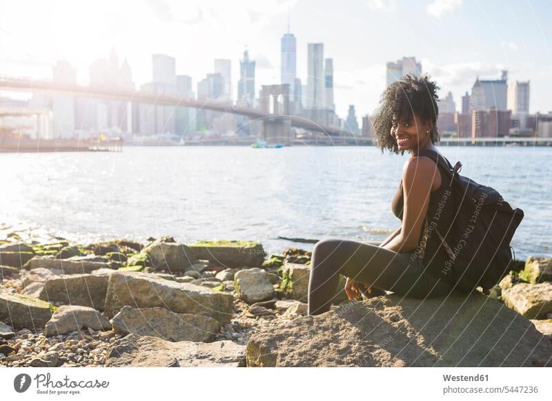 USA, New York City, Brooklyn, portrait of smiling woman sitting at the waterfront females women Skyline Skylines Urban Skyline bridge bridges Seated smile