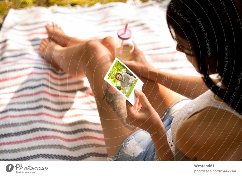 Young woman sitting on blanket looking at instant photo Seated females women photograph photographs photos eyeing Adults grown-ups grownups adult people persons