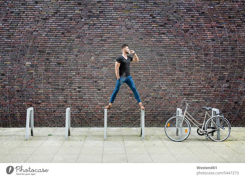 Man with cell phone balancing on bicycle rack in front of brick wall serious earnest Seriousness austere standing man men males mobile phone mobiles