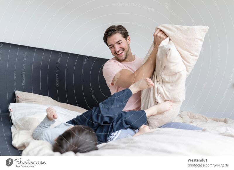 Happy father and son playing in bed cushion cushions pa fathers daddy dads papa sons manchild manchildren beds parents family families people persons