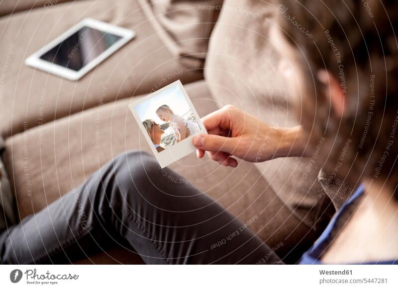Man sitting on couch looking at instant photo photograph photographs photos man men males settee sofa sofas couches settees image images picture pictures Adults
