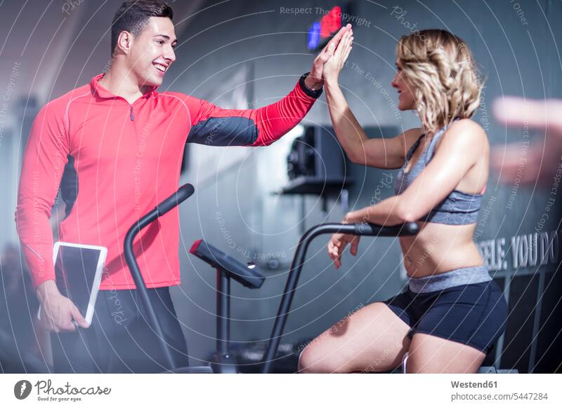 Fitness instrustor high fiving with woman on exercise machine coach coaches trainer exercising training practising gym gyms Health Club fitness sport sports