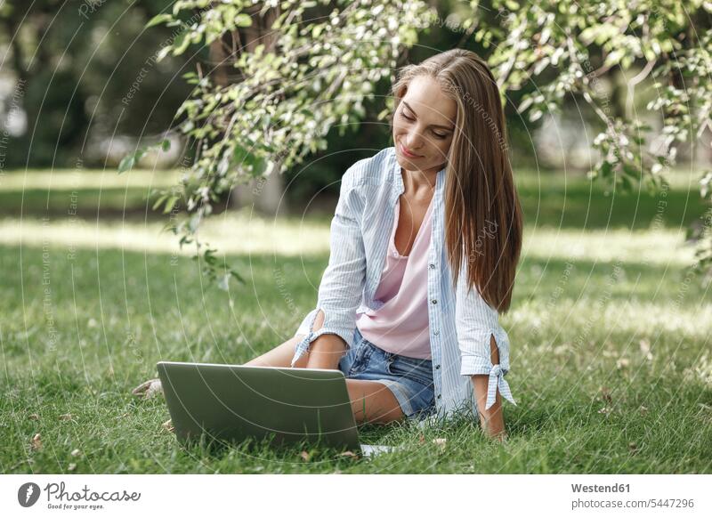 Young woman using laptop on a meadow smiling smile Laptop Computers laptops notebook females women park parks computer computers Adults grown-ups grownups adult