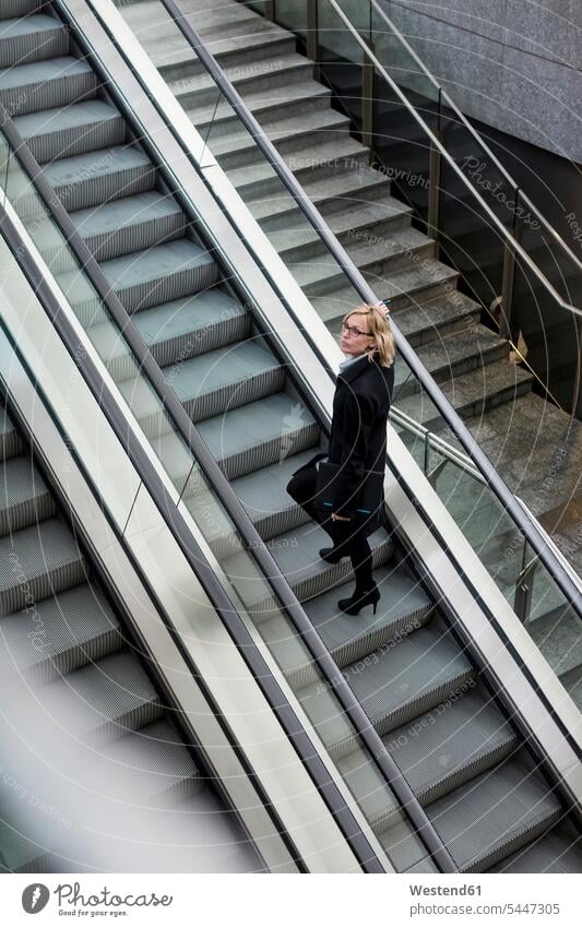 Businesswoman on escalator businesswoman businesswomen business woman business women moving staircase moving stairs Escalators business people businesspeople