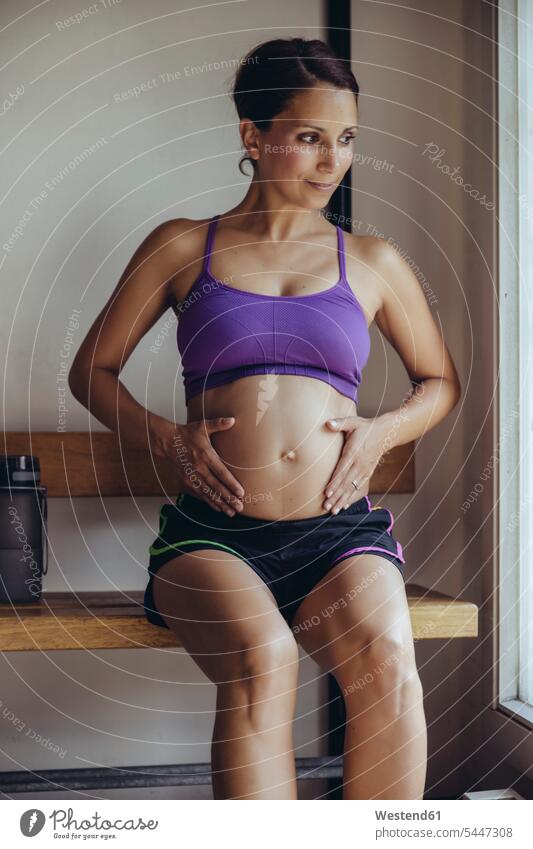 Sporty pregnant woman sitting in locker room Locker Room Dressing Room females women Pregnant Woman Seated smiling smile belly bellies abdomen human abdomen