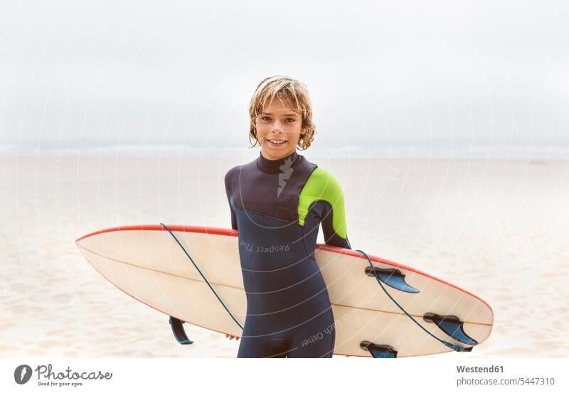 Spain, Aviles, portrait of smiling young surfer carrying surfboard on the beach sea ocean Teenager Teens teenagers beaches smile surfers surfboards water waters