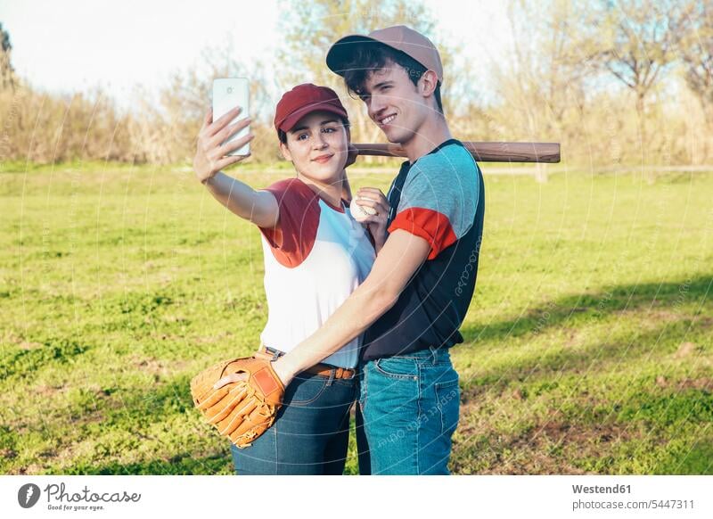 Smiling young couple with baseball equipment taking a selfie in park Selfie Selfies mobile phone mobiles mobile phones Cellphone cell phone cell phones smiling