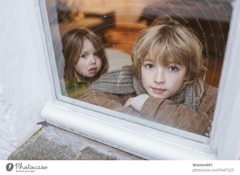 Portrait of boy looking out of window with his little sister in the background windows sisters watching siblings brother and sister brothers and sisters family