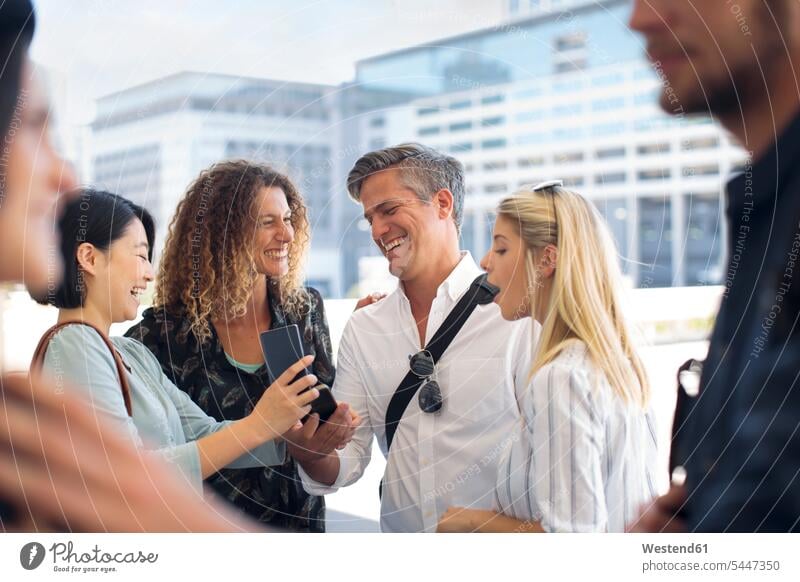 Group of happy casual businesspeople sharing cell phone on urban square mobile phone mobiles mobile phones Cellphone cell phones colleagues smiling smile