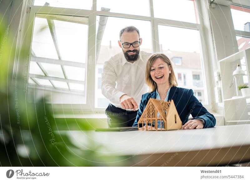 Laughing woman and man with house model in office businesswoman businesswomen business woman business women offices office room office rooms Businessman