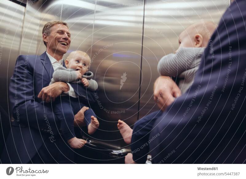 Happy mature businessman holding baby boy looking in mirror in elevator Businessman Business man Businessmen Business men infants nurselings babies father pa
