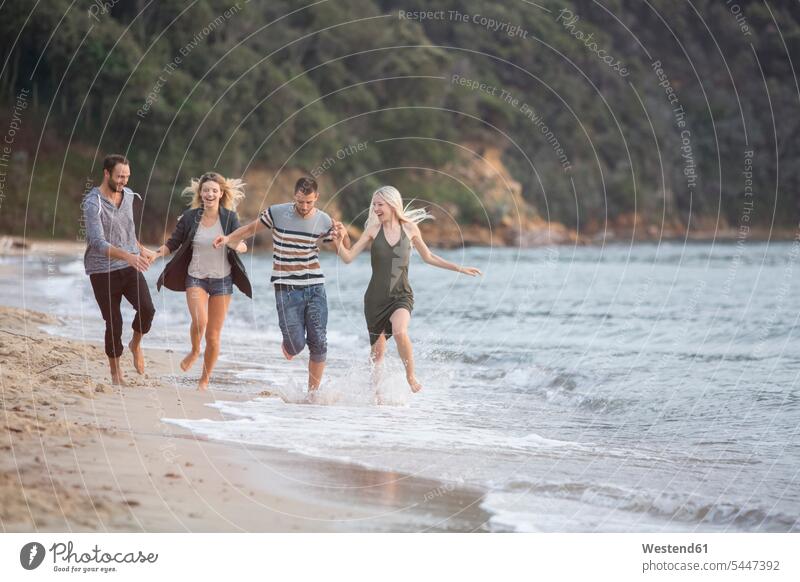 Four happy friends running at the beach laughing Laughter happiness Fun having fun funny positive Emotion Feeling Feelings Sentiments Emotions emotional