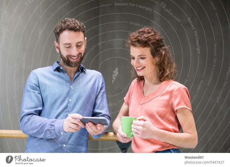 Man and woman in staircase with cell phone and cup of coffee mobile phone mobiles mobile phones Cellphone cell phones smiling smile colleagues concrete wall