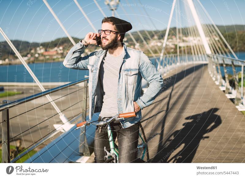 Young man with fixie bike on a bridge on the phone smiling smile call telephoning On The Telephone calling bicycle bikes bicycles mobile phone mobiles