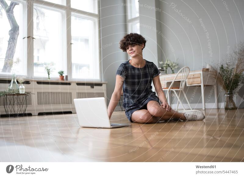 Young woman sitting on the floor at home looking at laptop females women Laptop Computers laptops notebook Adults grown-ups grownups adult people persons
