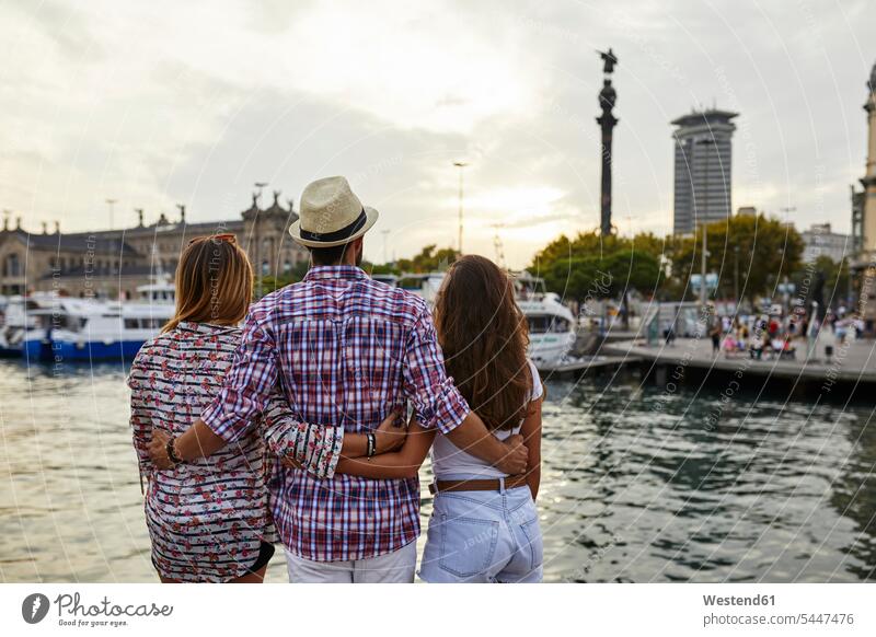 Spain, Barcelona, three tourists embracing at the waterfront in the city friends mate pier piers standing embrace Embracement hug hugging friendship tourism