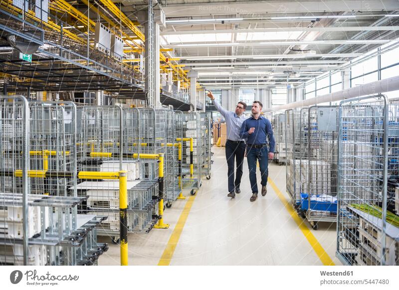 Two men walking and talking in factory shop floor man males factories speaking working At Work going Adults grown-ups grownups adult people persons human being