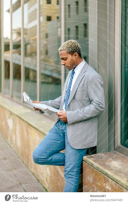 Businessman leaning against wall, reading newspaper standing Business man Businessmen Business men newspapers blond blond hair blonde hair business people