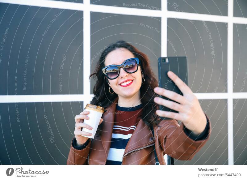 Portrait of smiling young woman with coffee to go taking selfie with smartphone Selfie Selfies females women Adults grown-ups grownups adult people persons