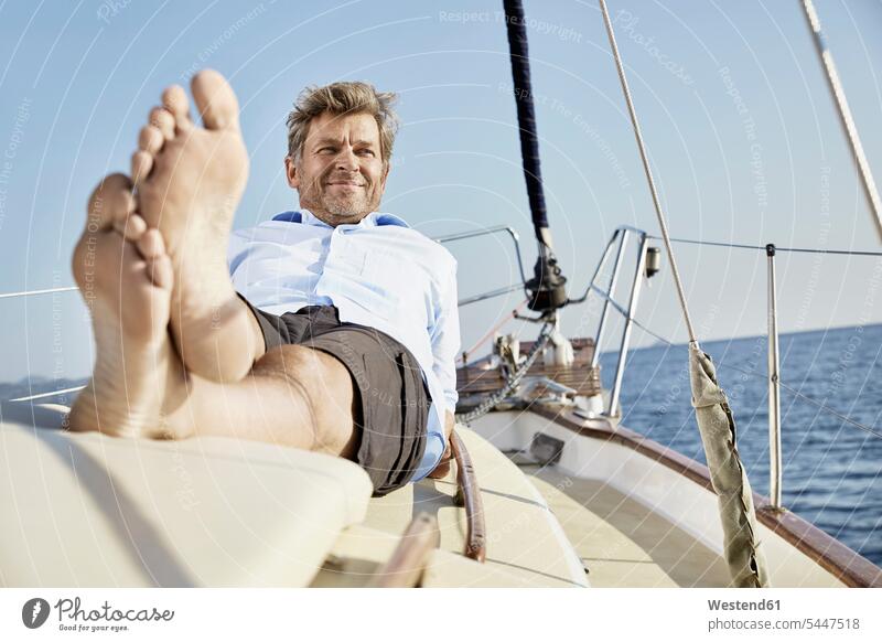 Portrait of smiling mature man lying on deck of his sailing boat men males portrait portraits Adults grown-ups grownups adult people persons human being humans