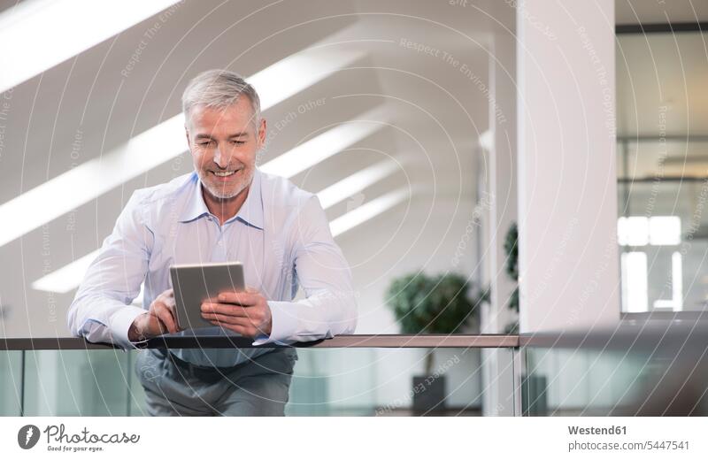 Successful businessman standing at railing in his office, using digital tablet offices office room office rooms Businessman Business man Businessmen