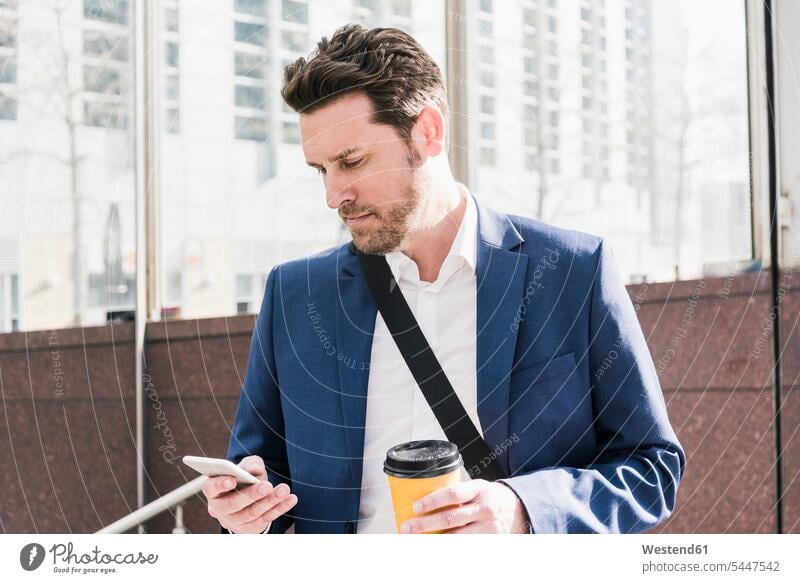 Businessman in the city, reading smart phone messages and holding cup of coffee Smartphone iPhone Smartphones mobile phone mobiles mobile phones Cellphone