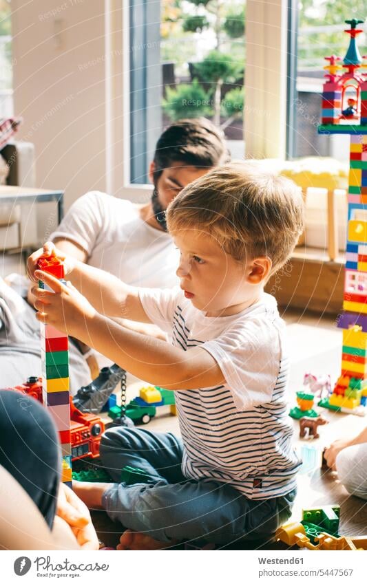 Boy with his family stacking building blocks on the floor playing families boy boys males people persons human being humans human beings child children kid kids