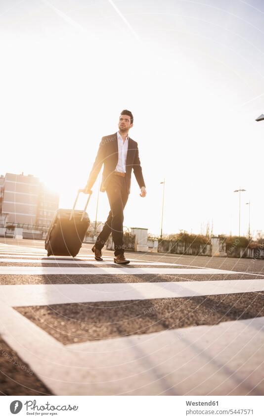 Businessman with rolling suitcase at sunset Business man Businessmen Business men business people businesspeople business world business life males walking