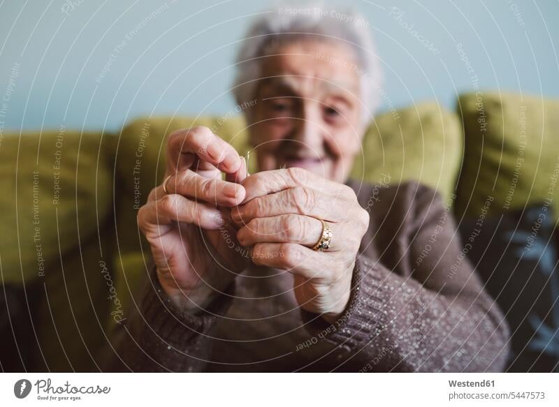 Hands of senior woman sitting on couch passing thread through buttonhole of sewing needle threading threads hand human hand hands human hands people persons