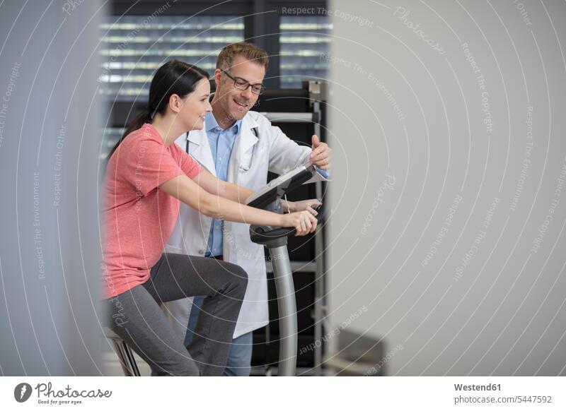 Smiling doctor and patient on exercise machine smiling smile exercise machines stationary bike Stationary Bikes fit practice physicians doctors